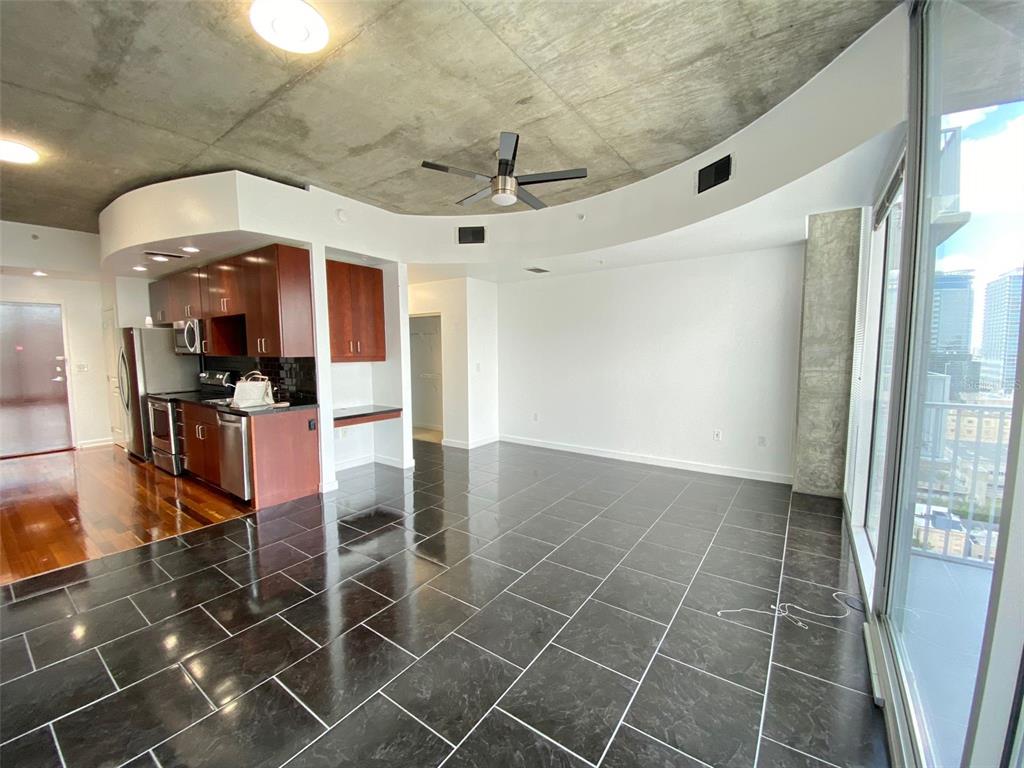 A modern apartment living area features a concrete ceiling, dark tile floors, and a kitchen — 155 S COURT AVENUE UNIT 1603, ORLANDO, FL