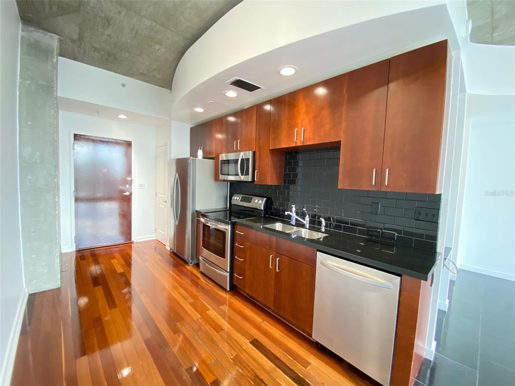 A modern kitchen features dark wood cabinets, black countertops, stainless steel appliances, and hardwood floors — 155 S COURT AVENUE UNIT 1603, ORLANDO, FL