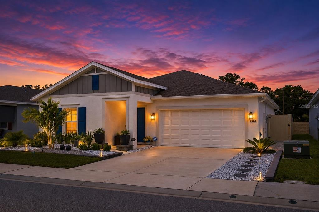 A single-story house with a two-car garage and landscaped front yard at sunset — 412 ADAMS ALE PLACE, DAVENPORT, FL