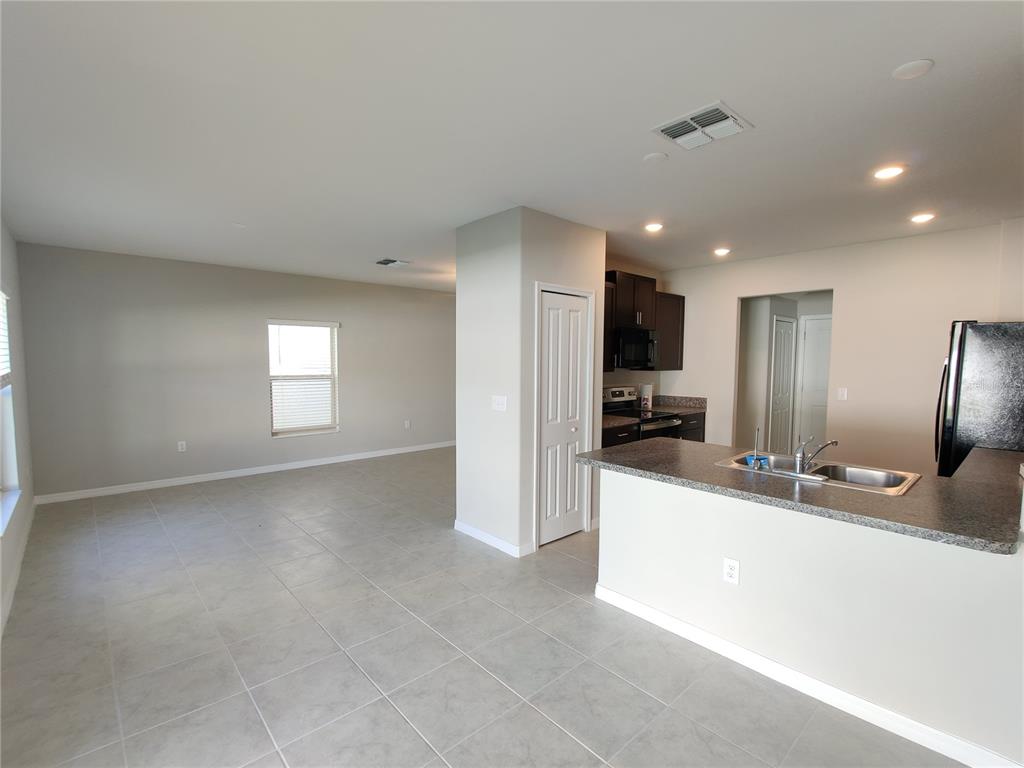 An open-concept kitchen with a breakfast bar overlooks a spacious living area with tile floors — 4710 NORMAN OAK PLACE, TAMPA, FL