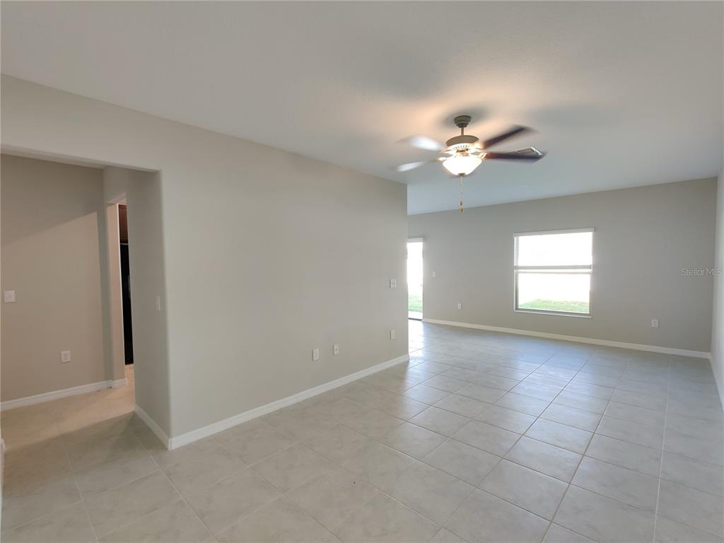 An open-concept living area features light-colored tile flooring, neutral walls, and a ceiling fan — 4710 NORMAN OAK PLACE, TAMPA, FL