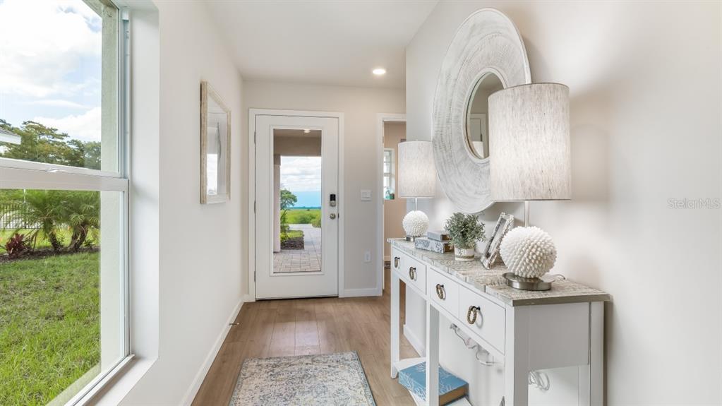 A bright entryway features light wood flooring, a white console table, and a glass-paneled door — 26229 SACRED LOTUS LANE, PUNTA GORDA, FL