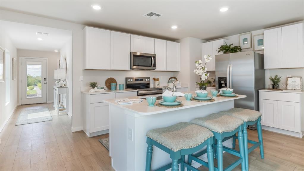 A kitchen with white cabinets, stainless steel appliances, a center island, and three teal stools — 26229 SACRED LOTUS LANE, PUNTA GORDA, FL