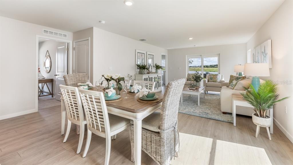 A dining area with a wooden table and chairs opens into a bright living room — 26229 SACRED LOTUS LANE, PUNTA GORDA, FL