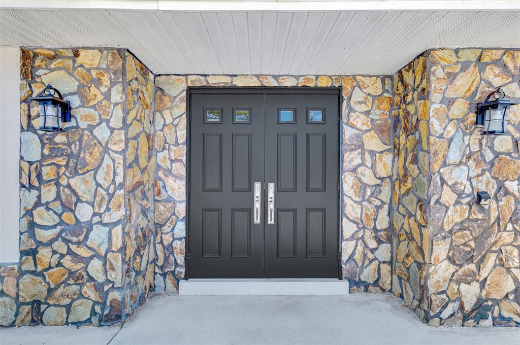 A dark double front door is flanked by stone walls and outdoor lanterns — 1620 MISSION VALLEY BOULEVARD, NOKOMIS, FL