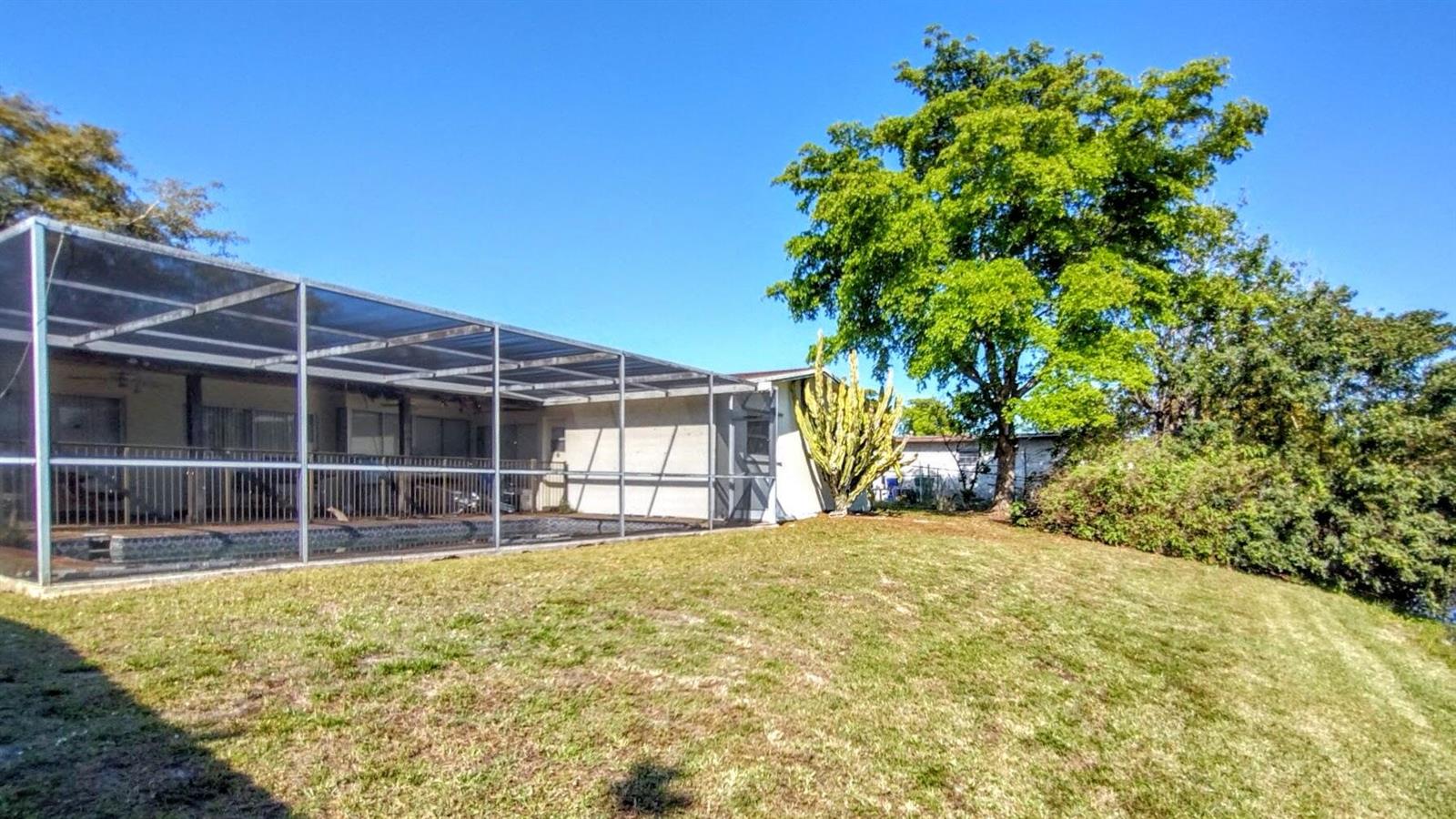 A backyard features a screened-in pool enclosure attached to a house next to a large tree — 8528 Windsor Drive, Miramar FL 33025, MIRAMAR, FL
