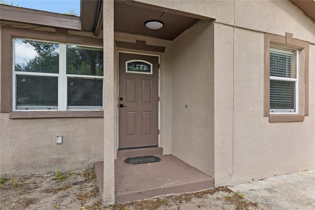 A brown front door is centered under a covered porch with two windows nearby — 540 COLFAX DRIVE, DAYTONA BEACH, FL