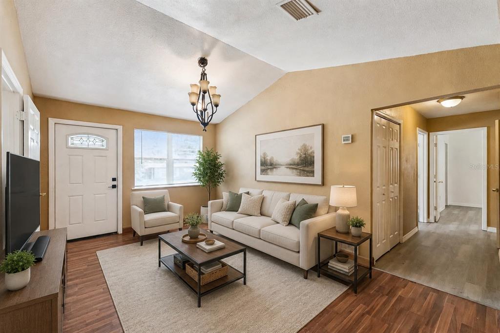 A living room features a vaulted ceiling, beige walls, wood-look flooring, and a neutral sofa — 540 COLFAX DRIVE, DAYTONA BEACH, FL