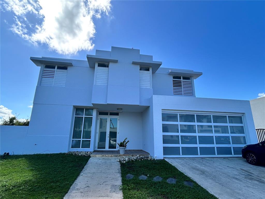 A two-story white modern house features a glass-paneled garage door and a front entryway — 345 CALLE TULIPAN, CAGUAS, PR
