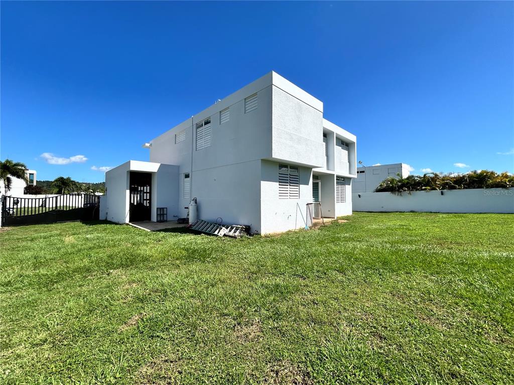 A two-story white concrete house stands on a large grassy lot under a blue sky — 345 CALLE TULIPAN, CAGUAS, PR