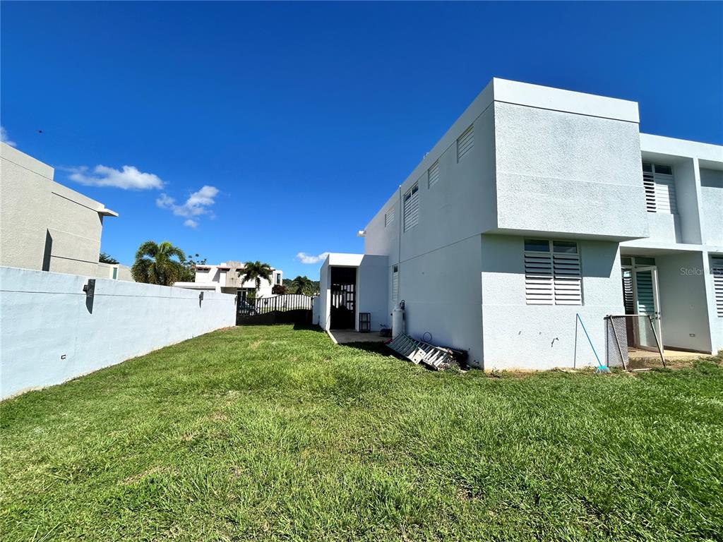 The exterior of a white two-story house features a grassy backyard and a side patio — 345 CALLE TULIPAN, CAGUAS, PR
