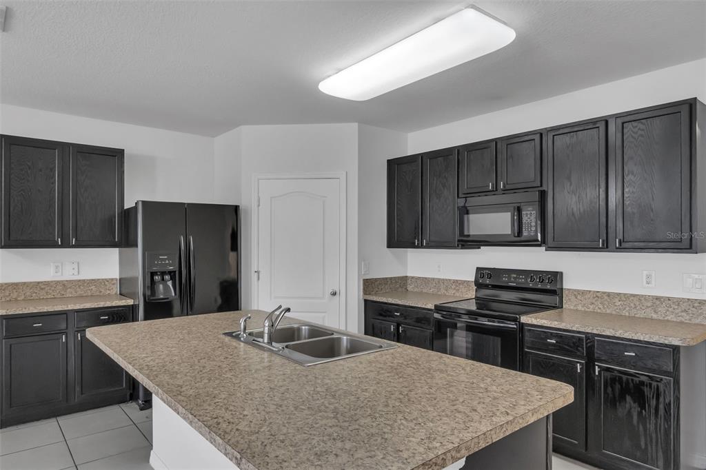 A kitchen features dark cabinetry, tan laminate countertops, a center island, and black appliances — 1828 PARTIN TERRACE ROAD, KISSIMMEE, FL