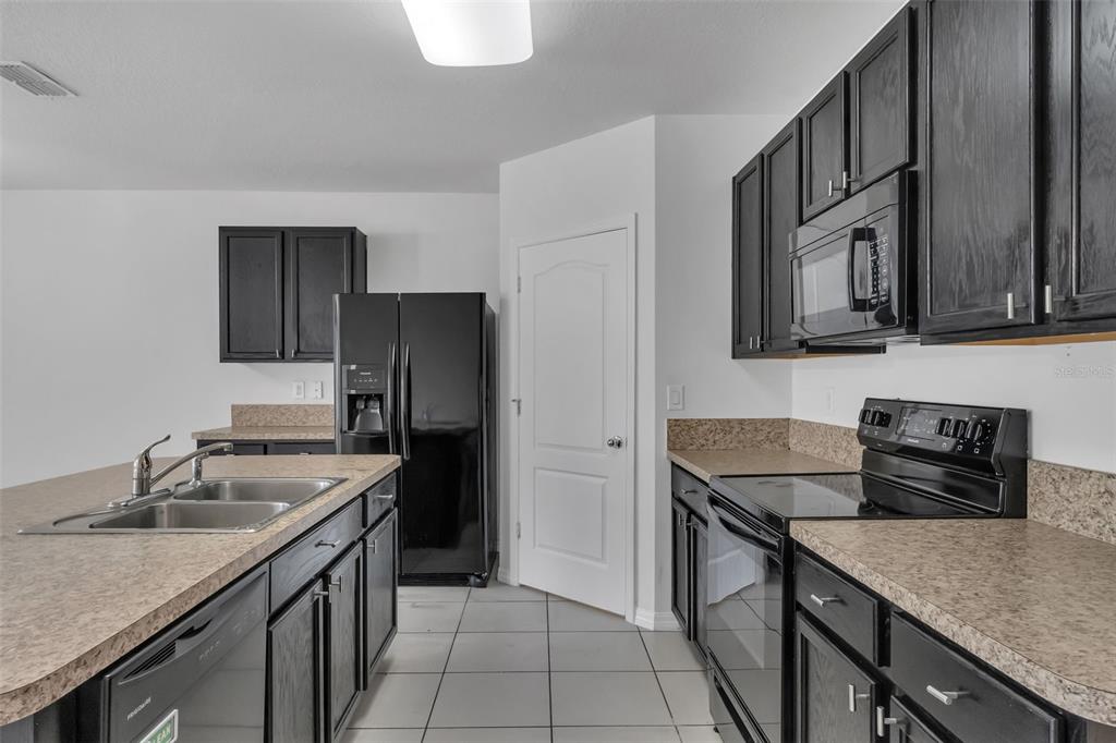 A kitchen featuring dark wood cabinets, black appliances, and tan laminate countertops — 1828 PARTIN TERRACE ROAD, KISSIMMEE, FL