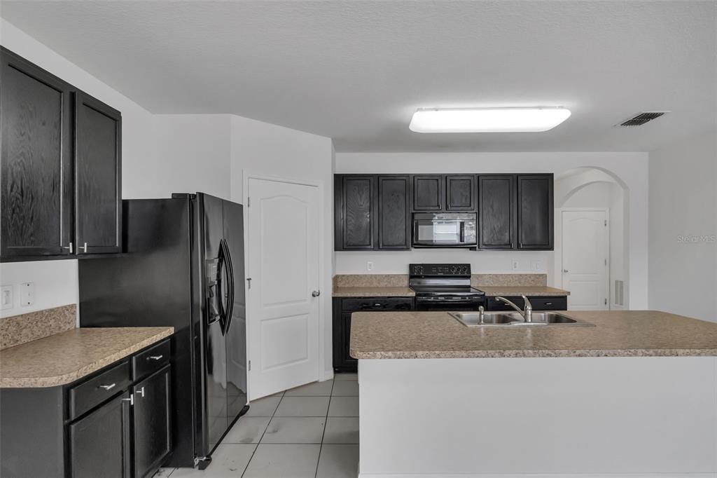 A kitchen features dark wood cabinets, laminate countertops, black appliances, and a central island — 1828 PARTIN TERRACE ROAD, KISSIMMEE, FL