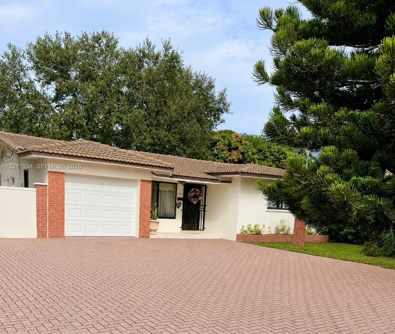 A single-story house features a white stucco exterior, a brick-accented garage, and a paved driveway — 6385 SW 25th St, Miami FL 33155, MIAMI, FL