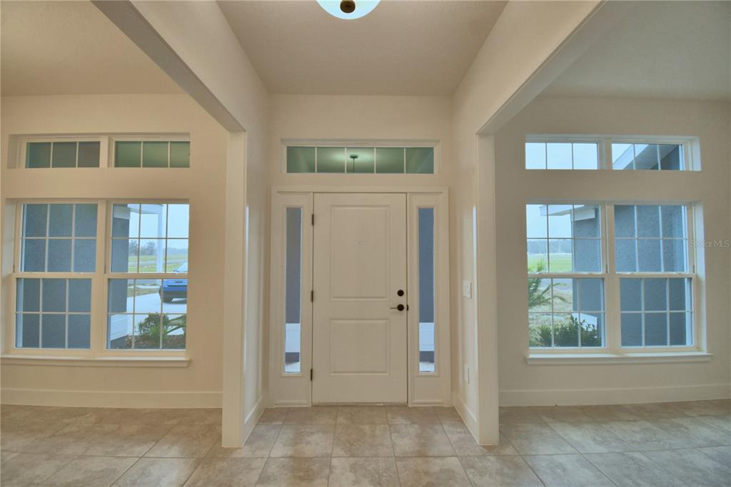 An entryway features a white front door with sidelights, large windows, and tiled flooring — 4611 CALAMINT LANE, AUBURNDALE, FL