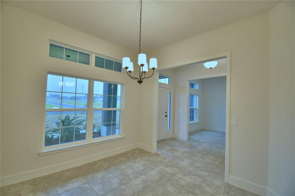 A dining area features tile flooring, a chandelier, and large windows overlooking an empty lot — 4611 CALAMINT LANE, AUBURNDALE, FL