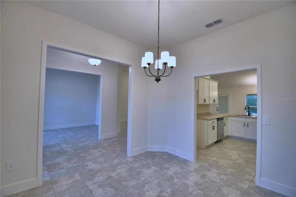 A dining area with a chandelier, tile flooring, and doorways leading to a kitchen and room — 4611 CALAMINT LANE, AUBURNDALE, FL