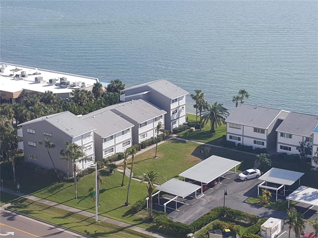 An aerial view shows multi-story apartment buildings with covered parking spaces near a body of water — 1301 GULF BOULEVARD UNIT 101, CLEARWATER BEACH, FL