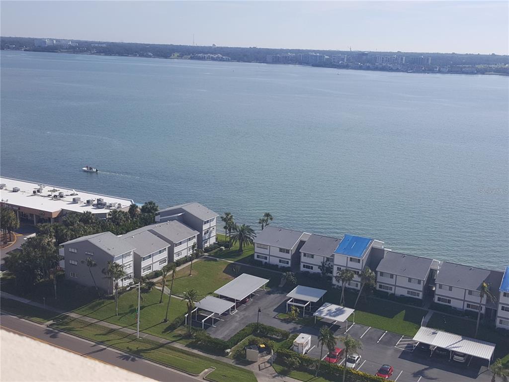 An aerial view of a waterfront apartment complex with parking carports and a boat nearby — 1301 GULF BOULEVARD UNIT 101, CLEARWATER BEACH, FL