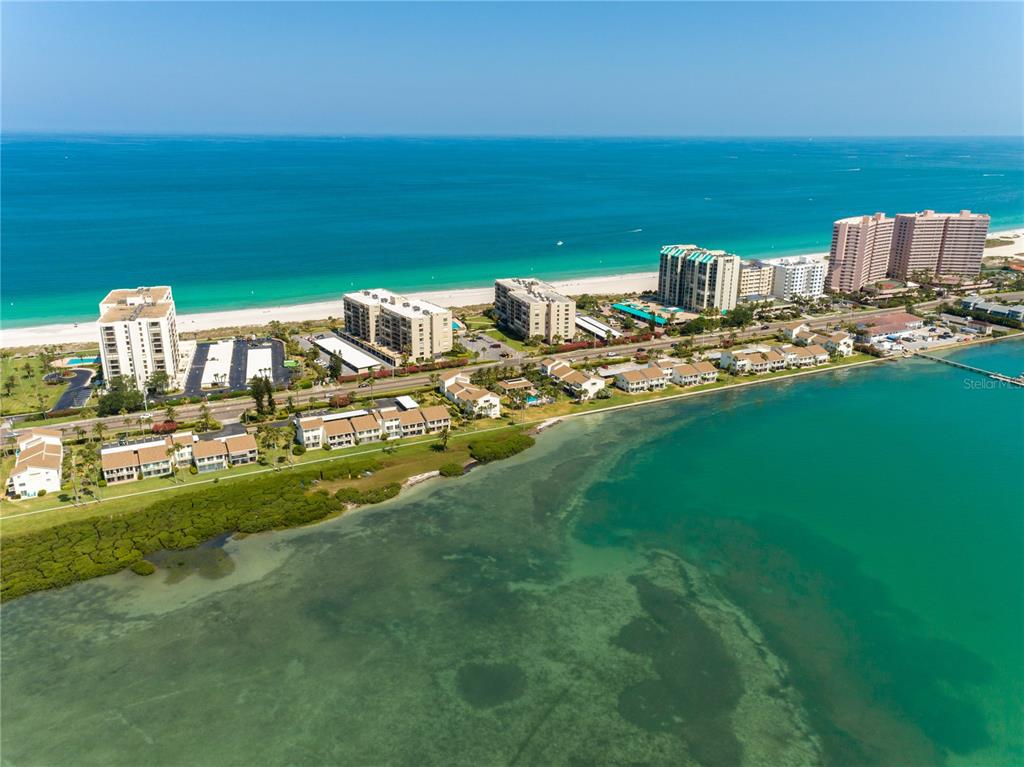 An aerial view shows a coastal area with multi-story buildings, a beach, and a bay — 1301 GULF BOULEVARD UNIT 101, CLEARWATER BEACH, FL