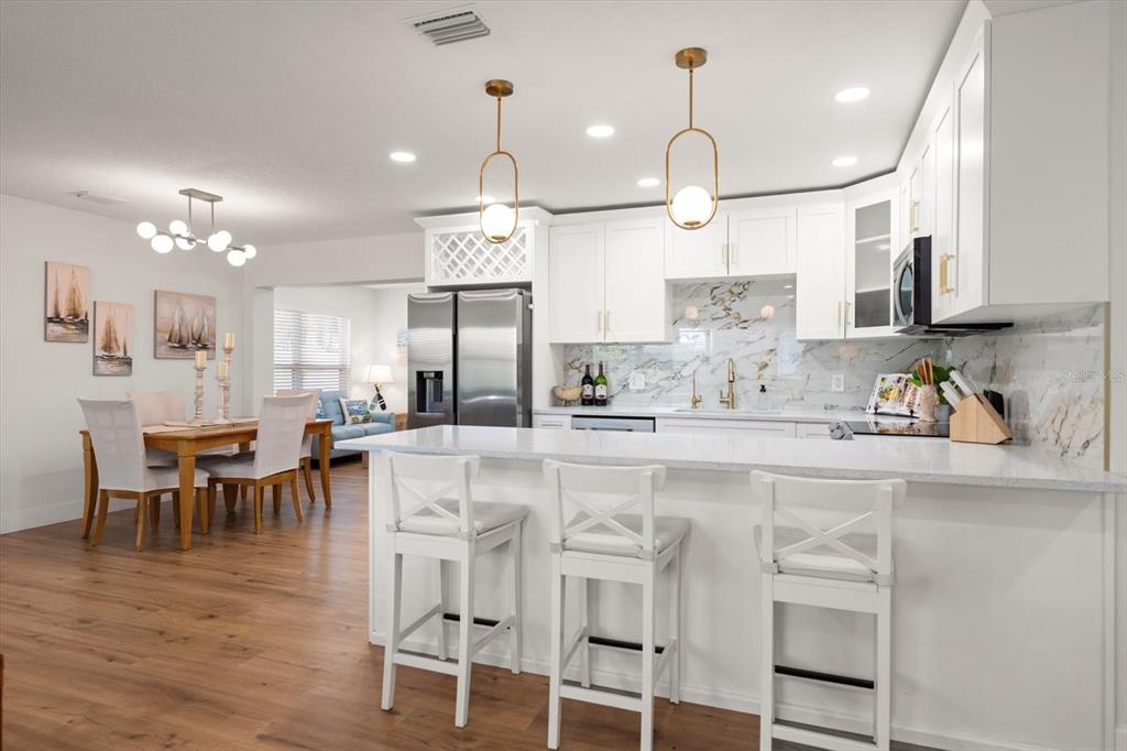 A modern kitchen with white cabinets, marble-style backsplash, and a breakfast bar with three stools — 8879 111TH STREET, SEMINOLE, FL