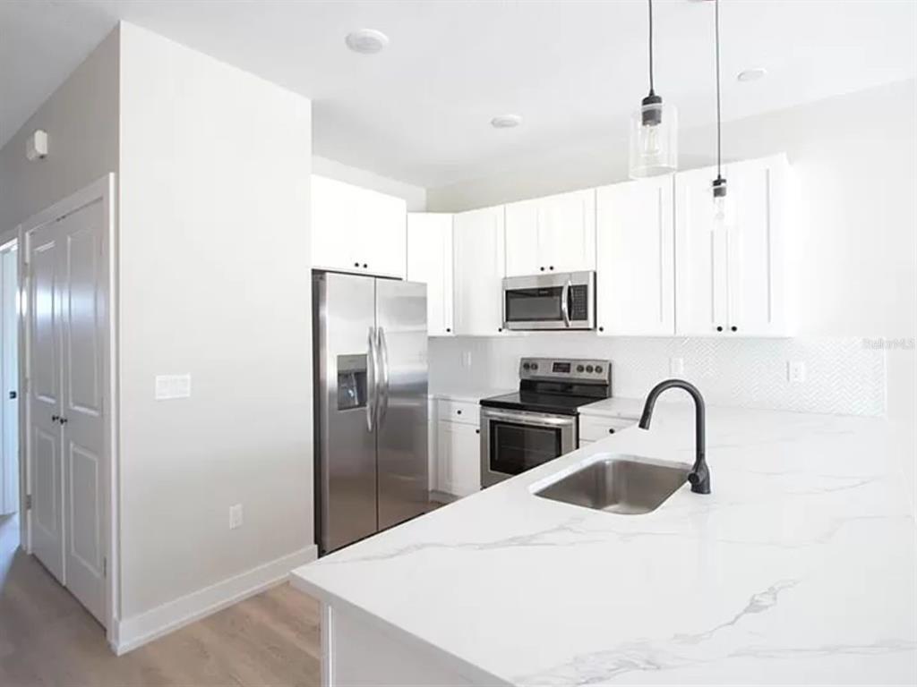 A modern kitchen features white cabinets, stainless steel appliances, and a marble-patterned island countertop — 9285 AGATE STREET, PORT CHARLOTTE, FL