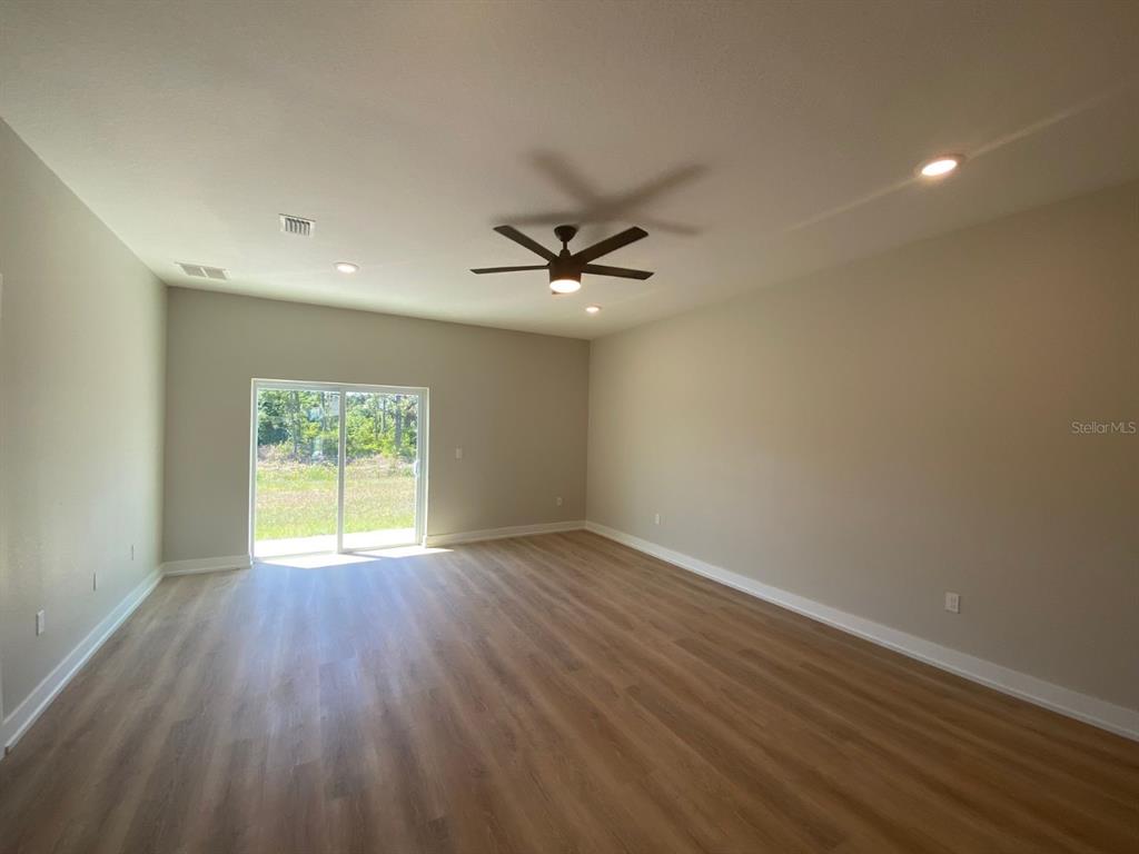 An empty room features light wood-look flooring, neutral walls, a ceiling fan, and sliding doors — 9285 AGATE STREET, PORT CHARLOTTE, FL