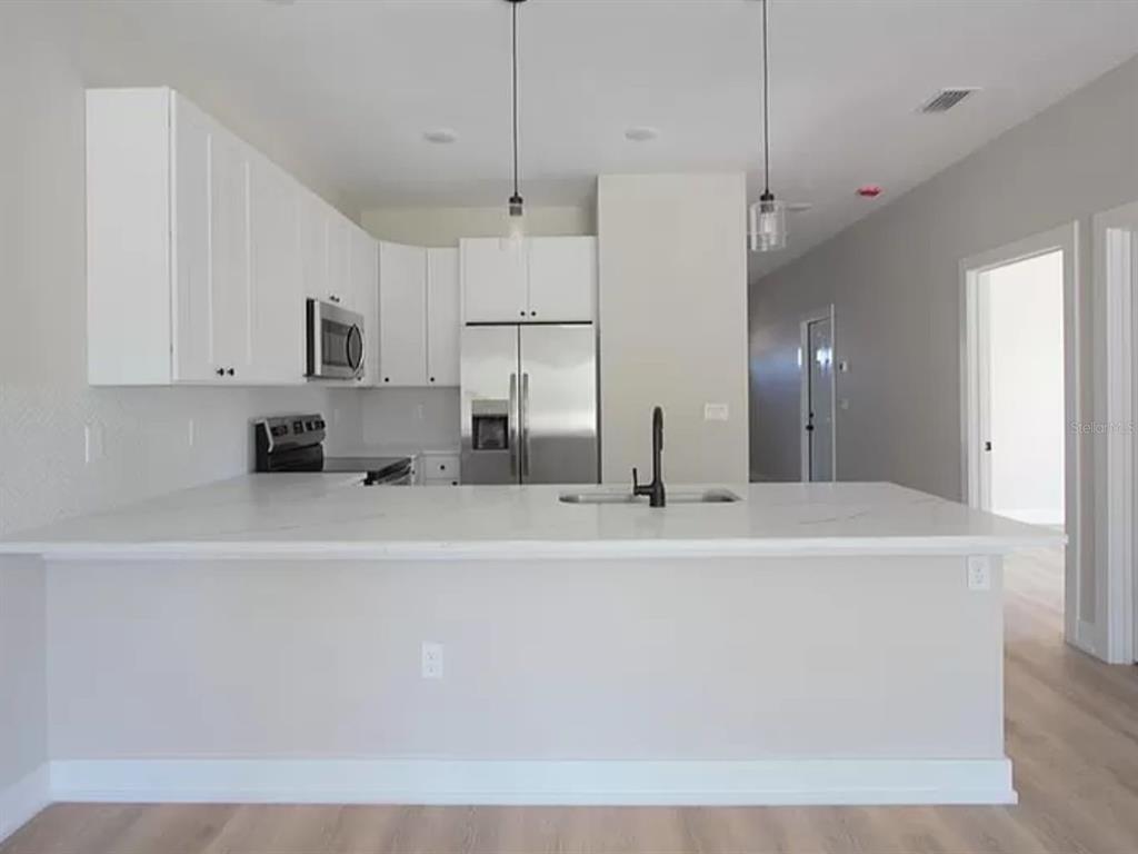 A kitchen features white cabinets, stainless steel appliances, and a white countertop island — 9285 AGATE STREET, PORT CHARLOTTE, FL
