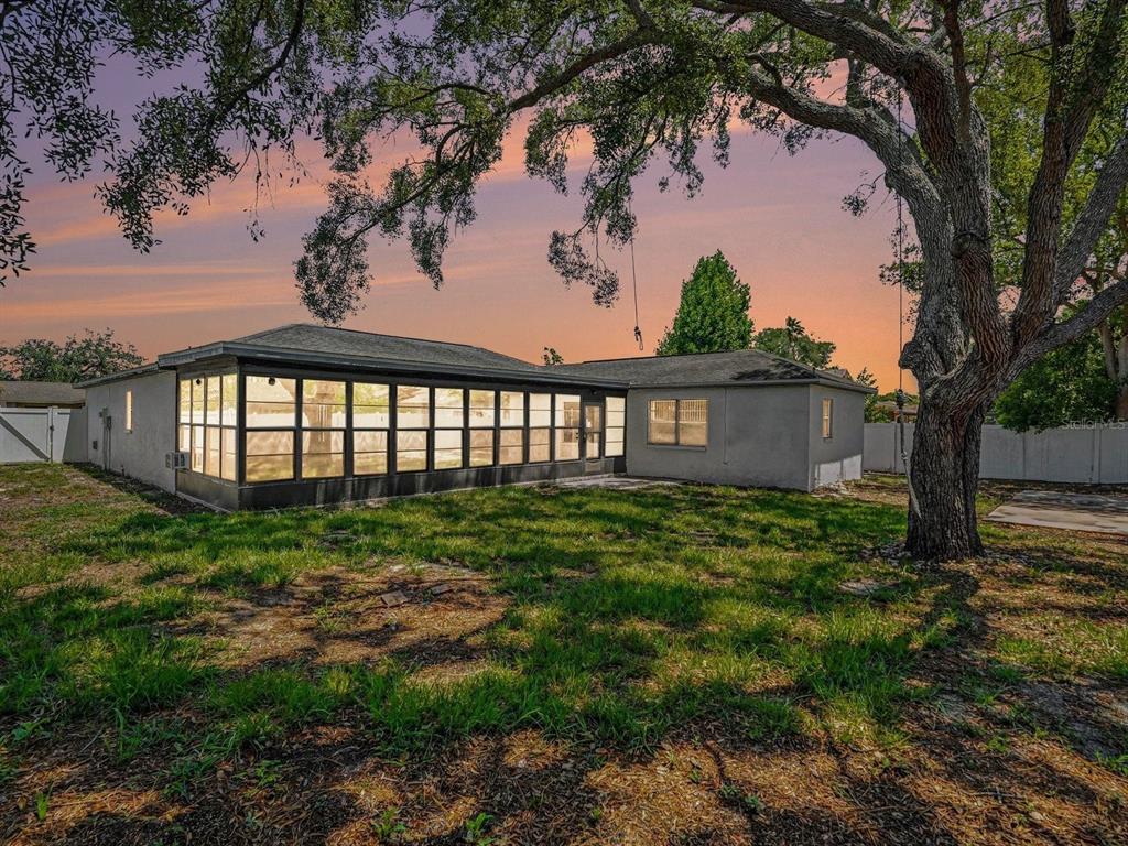 A backyard view of a house with a large enclosed sunroom and a mature tree — 8180 WOODEN DRIVE, SPRING HILL, FL