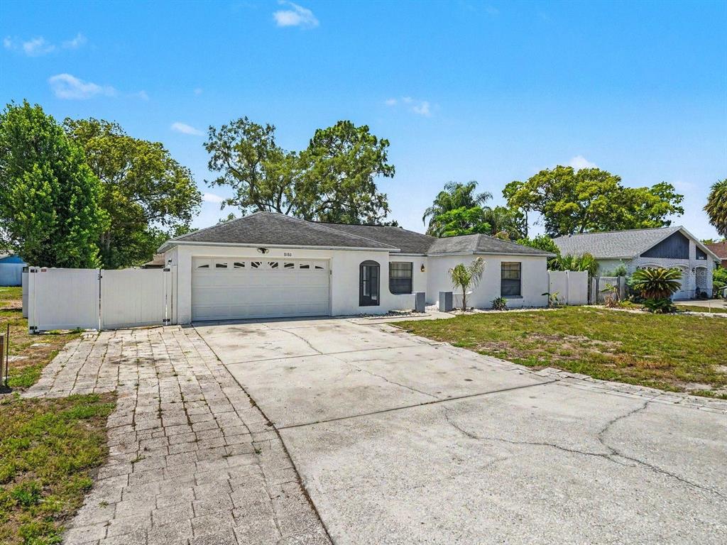 A single-story white house with a two-car garage and a paved driveway — 8180 WOODEN DRIVE, SPRING HILL, FL