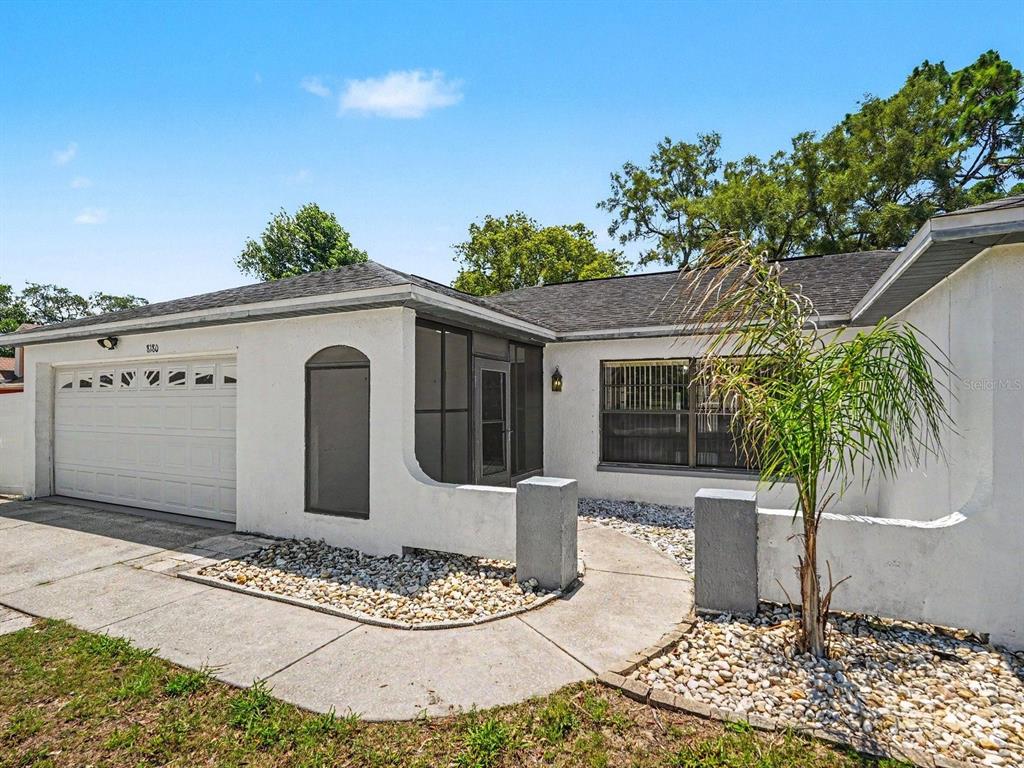 A white single-story house with a garage, a screened entryway, and a rock-covered front yard — 8180 WOODEN DRIVE, SPRING HILL, FL