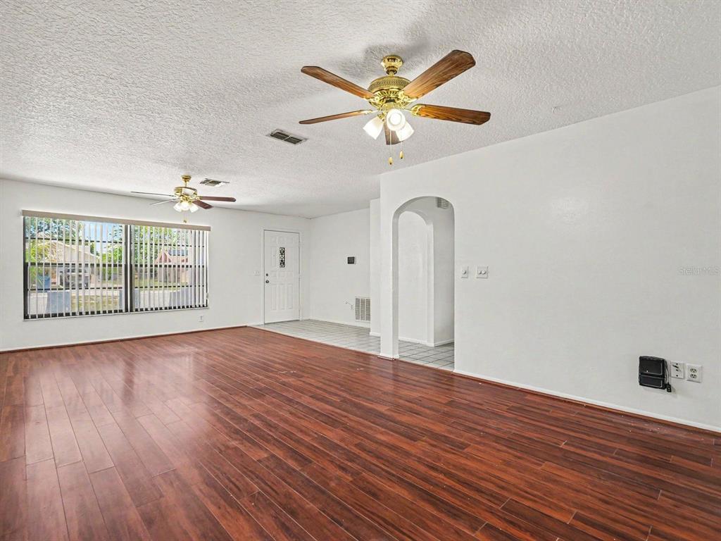 A living room with wood-look flooring, two ceiling fans, and an arched entryway — 8180 WOODEN DRIVE, SPRING HILL, FL