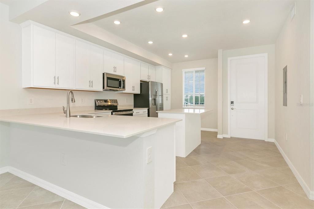 A modern kitchen features white cabinetry, stainless steel appliances, and a large quartz-topped island — 12320 WELLEN GOLF STREET UNIT 305, VENICE, FL