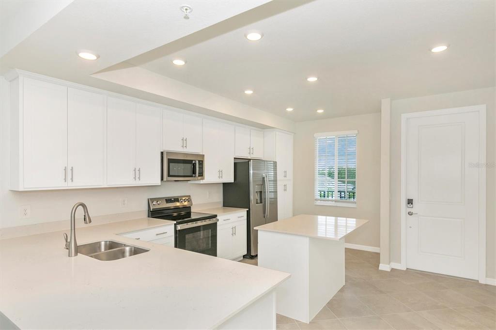 A modern kitchen features white cabinetry, stainless steel appliances, and a quartz-topped island — 12320 WELLEN GOLF STREET UNIT 305, VENICE, FL