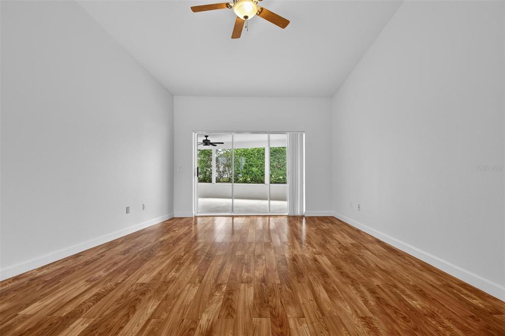 A bright, empty room features wood-look flooring, white walls, a ceiling fan, and sliding glass doors — 231 WELLINGTON DRIVE, PALM COAST, FL