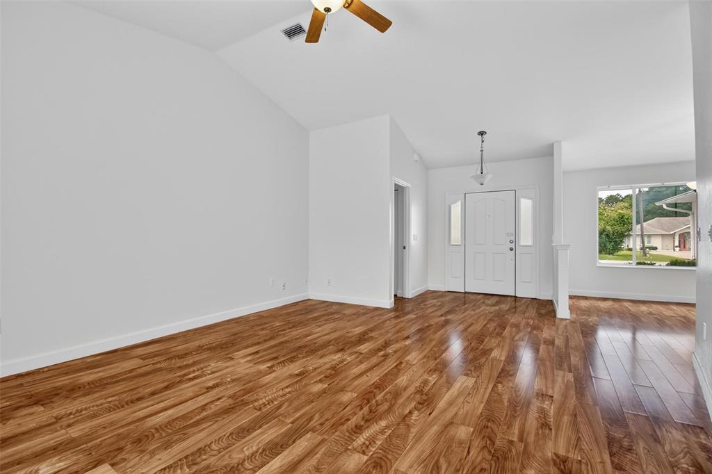 An empty living room features light gray walls, vaulted ceilings, and wood-look laminate flooring — 231 WELLINGTON DRIVE, PALM COAST, FL
