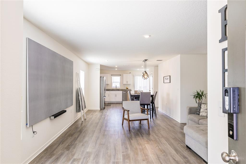 An open-concept living and dining area features light wood-look flooring and white kitchen cabinets — 2234 MAJESTIC SPAN AVENUE, EAGLE LAKE, FL