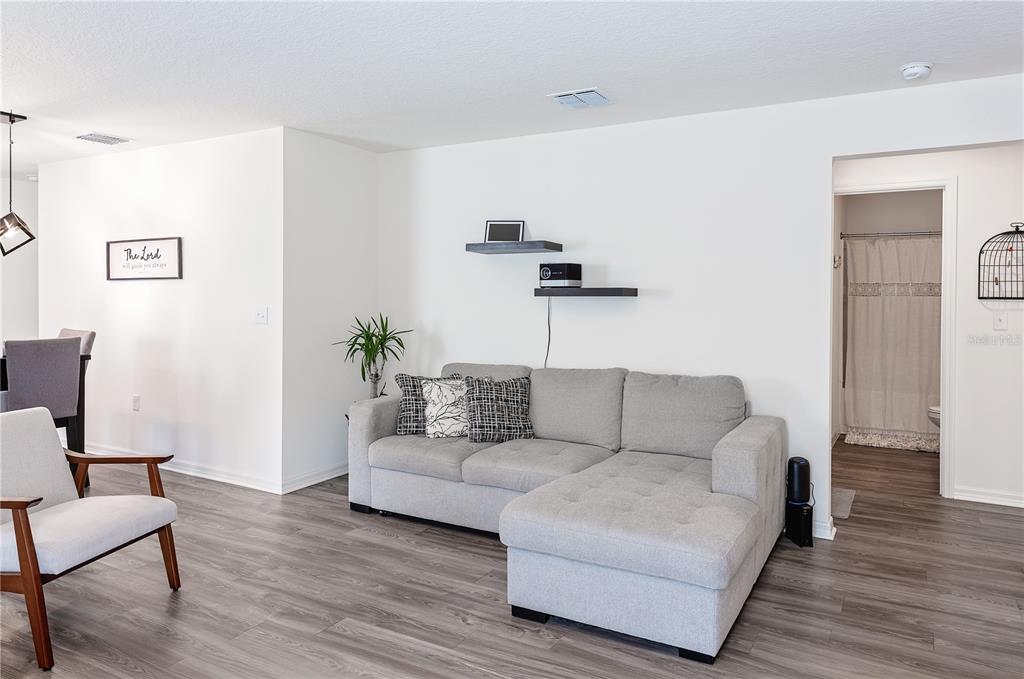 A living room features a gray sectional sofa, floating shelves, and light wood-look flooring — 2234 MAJESTIC SPAN AVENUE, EAGLE LAKE, FL