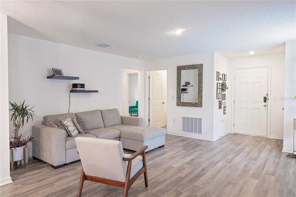A living room features light gray wood-look flooring, a sectional sofa, and a white front door — 2234 MAJESTIC SPAN AVENUE, EAGLE LAKE, FL