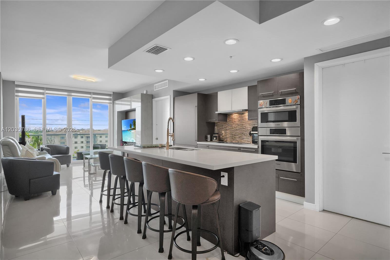 A modern kitchen features a large island with bar seating and stainless steel built-in appliances — 7751 NW 107th Ave # 701, Doral FL 33178, DORAL, FL