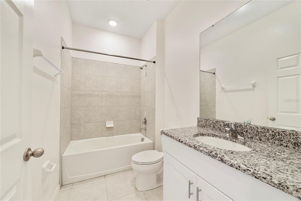 A bathroom features a white vanity with granite countertops, a toilet, and a tiled tub-shower — 662 FAIRVIEW AVENUE, HAINES CITY, FL