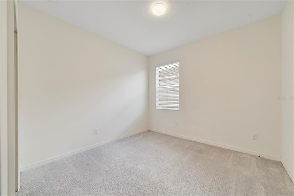 An empty bedroom features beige walls, light gray carpeting, a single window, and a ceiling light — 662 FAIRVIEW AVENUE, HAINES CITY, FL