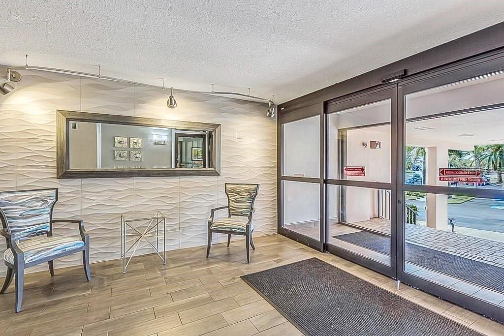 A lobby features a textured wall, a large mirror, two chairs, and sliding glass doors — 51 ISLAND WAY UNIT 108, CLEARWATER BEACH, FL