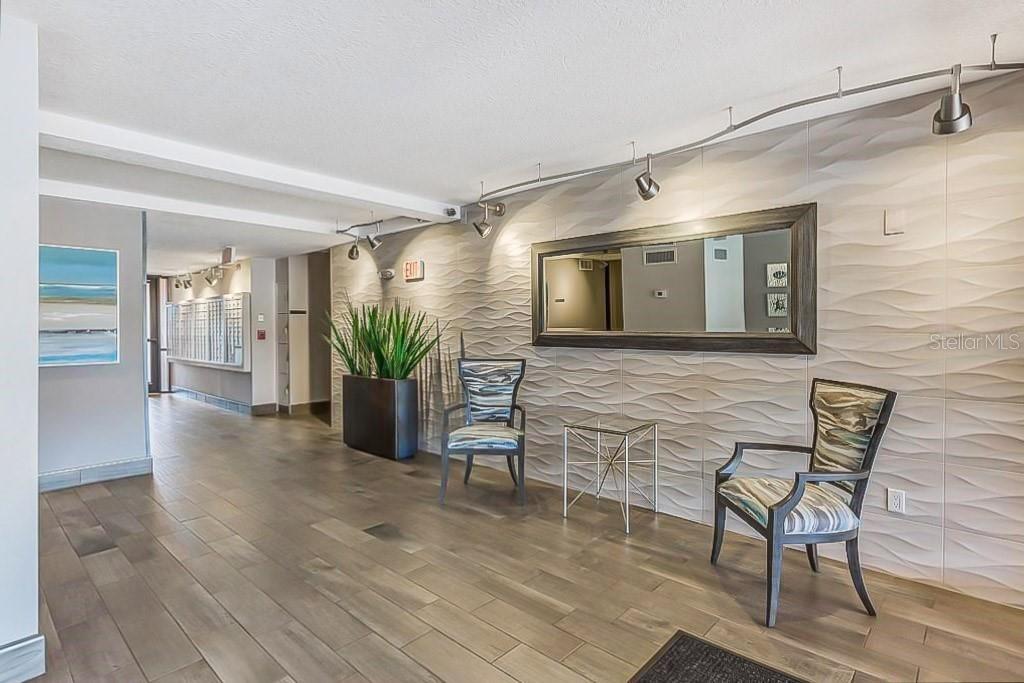 A modern building lobby features textured wall tiles, a large mirror, and two patterned chairs — 51 ISLAND WAY UNIT 108, CLEARWATER BEACH, FL