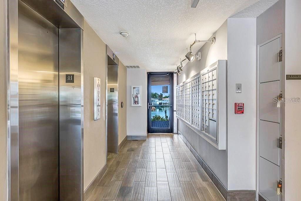 A hallway features two elevators, a wall of mailboxes, and a glass door to outside — 51 ISLAND WAY UNIT 108, CLEARWATER BEACH, FL