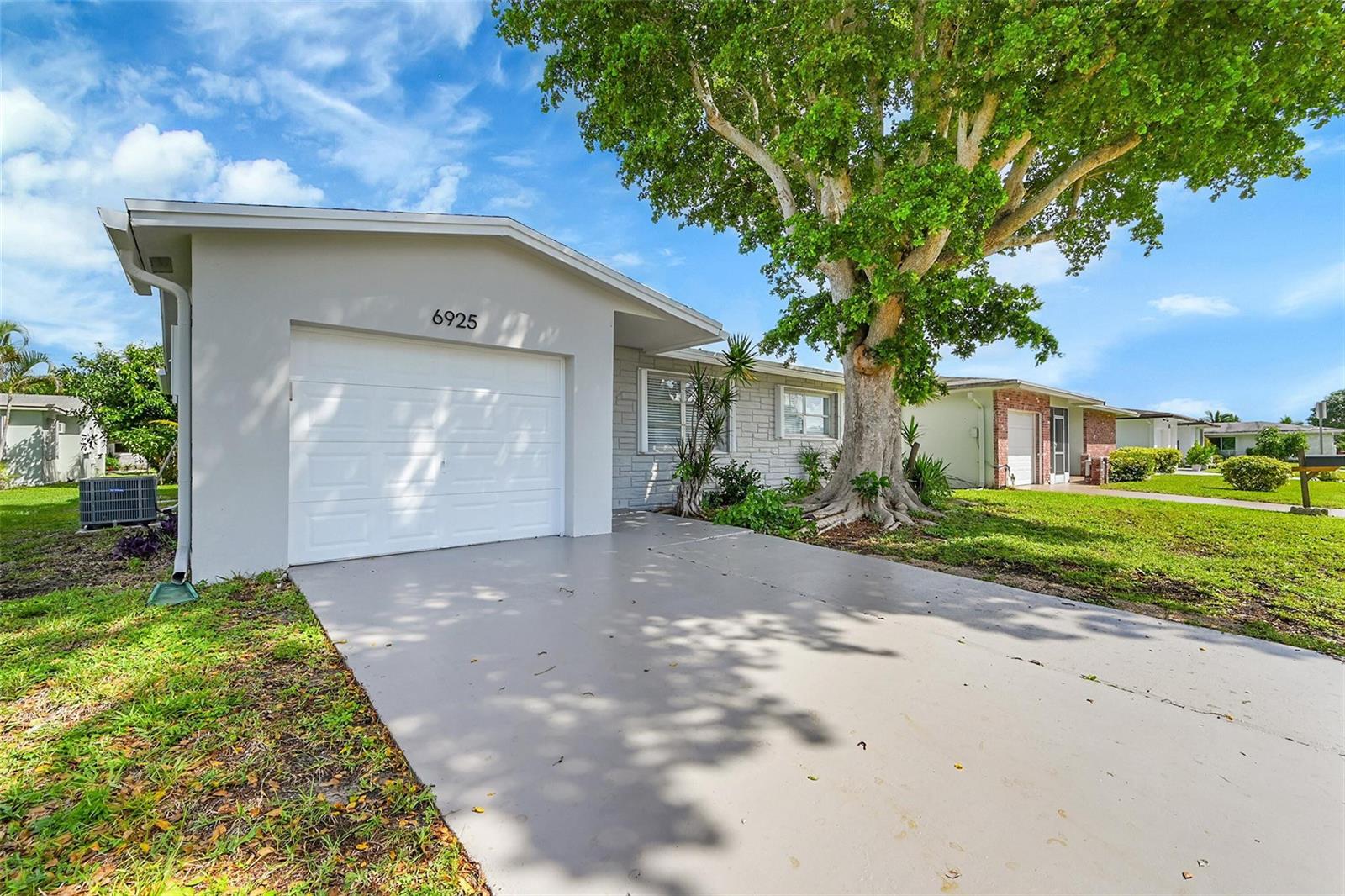 A single-story house with a white garage, gray stone siding, and a large shade tree — 6925 NW 11th Street, Margate FL 33063, MARGATE, FL