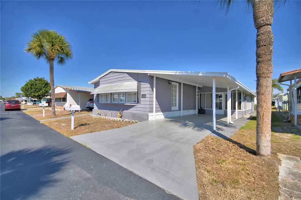 A single-story manufactured home with a concrete driveway, carport, and palm trees under a blue sky — 4321 CHERRYWOOD STREET, WINTER HAVEN, FL