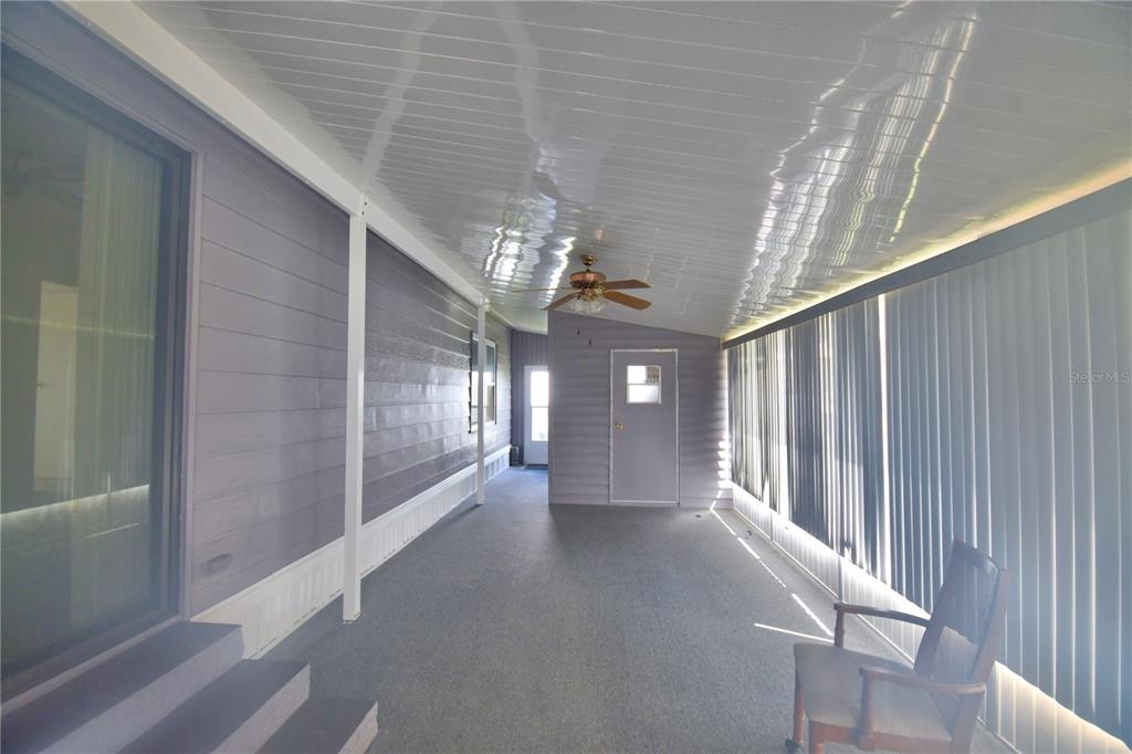 A covered porch features gray siding, a ceiling fan, carpeted flooring, and vertical window blinds — 4321 CHERRYWOOD STREET, WINTER HAVEN, FL