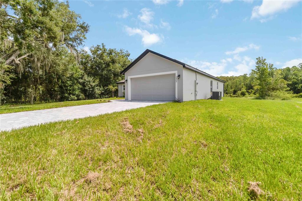 A light gray house with a two-car garage sits on a grassy lot with trees — 3525 RAMBLER AVENUE, ST CLOUD, FL